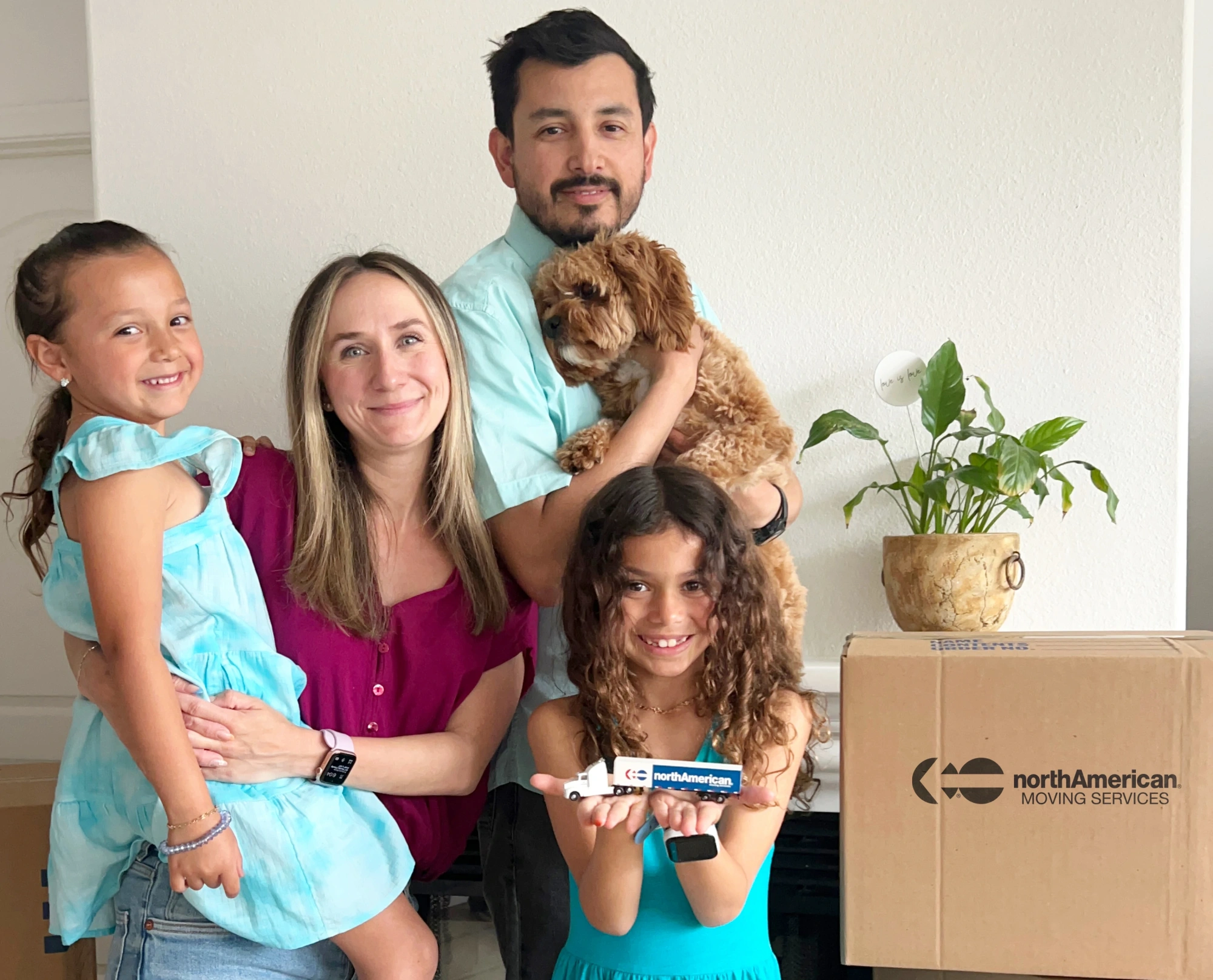 Mother, father, two kids, and dog in front of North American Van Lines packing boxes