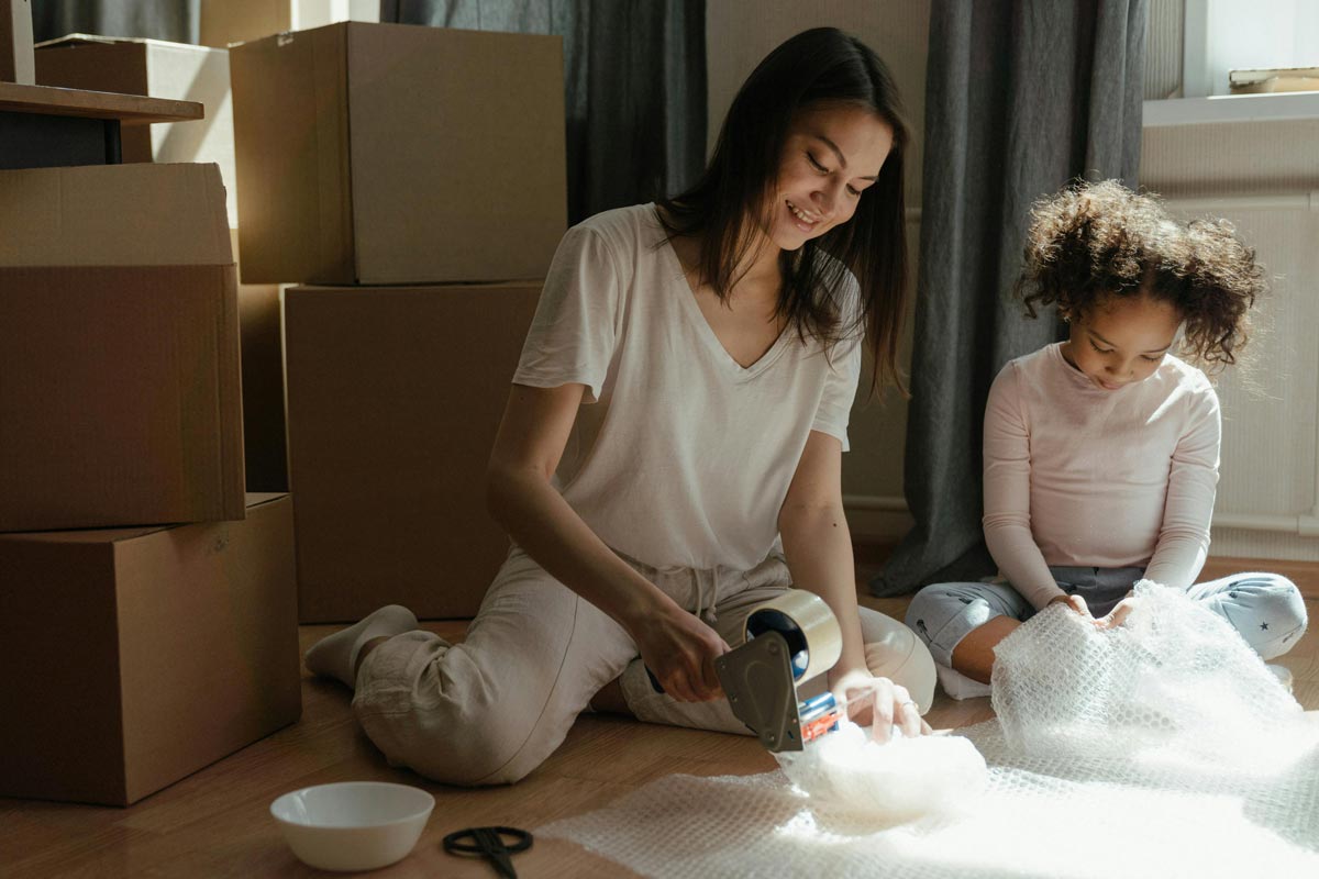 Mother and daughter sitting on the floor with wrapping bowls for the move